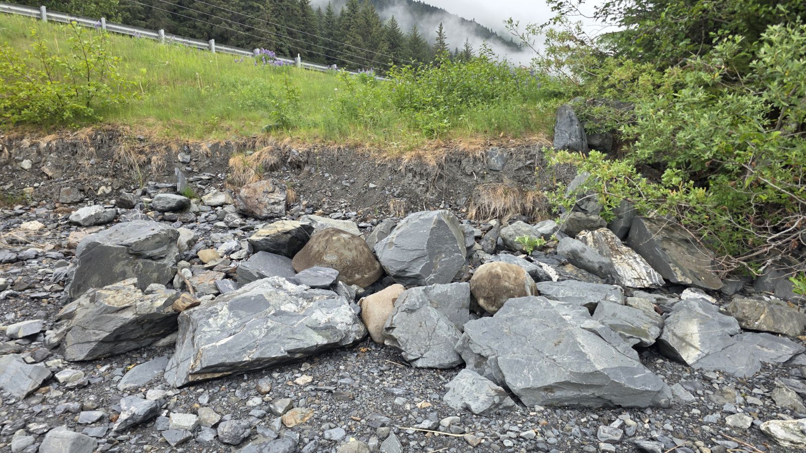 Wide view of the riprap bank meeting the gravel and silt of the tidal flats below the Seward Highway.